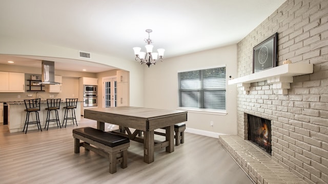 dining area with light hardwood / wood-style flooring, a chandelier, and a brick fireplace