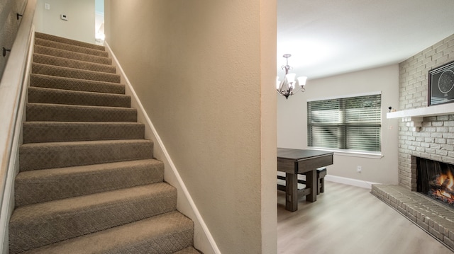 stairway featuring a notable chandelier, wood-type flooring, and a fireplace