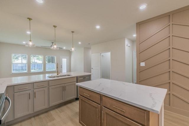 kitchen featuring pendant lighting, sink, light wood-type flooring, light stone counters, and a center island