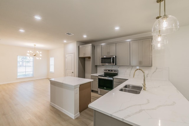 kitchen featuring appliances with stainless steel finishes, gray cabinetry, sink, decorative light fixtures, and a kitchen island