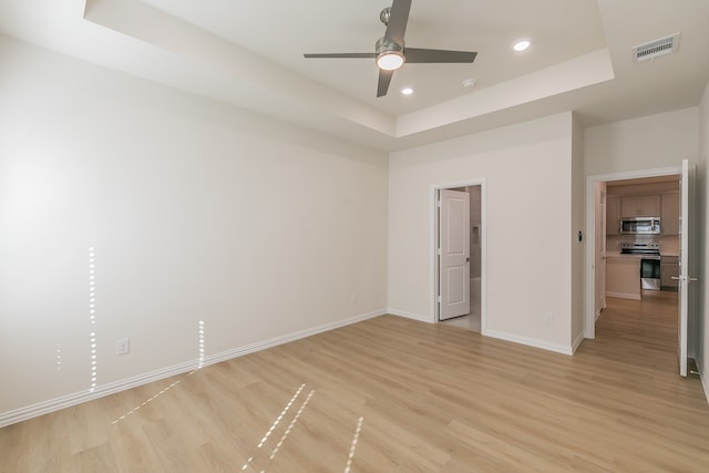 spare room with ceiling fan, light hardwood / wood-style flooring, and a tray ceiling