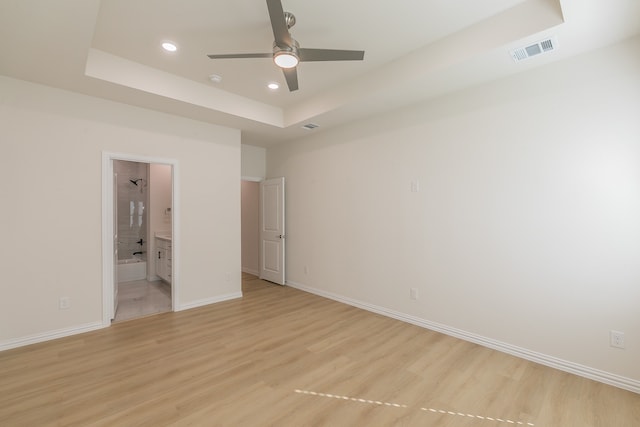 unfurnished bedroom featuring ceiling fan, light wood-type flooring, ensuite bath, and a tray ceiling