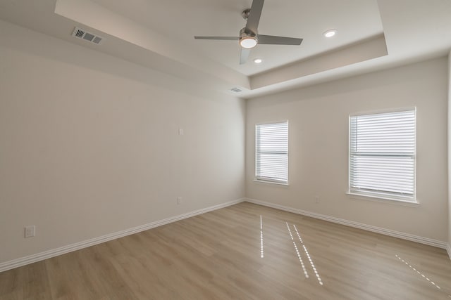 unfurnished room with ceiling fan, a raised ceiling, and light hardwood / wood-style flooring