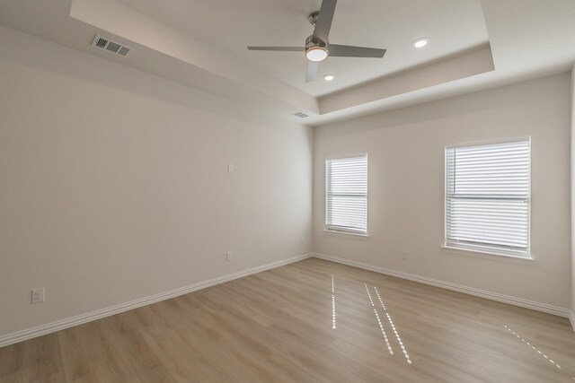 unfurnished room with light wood-type flooring, baseboards, visible vents, and a tray ceiling