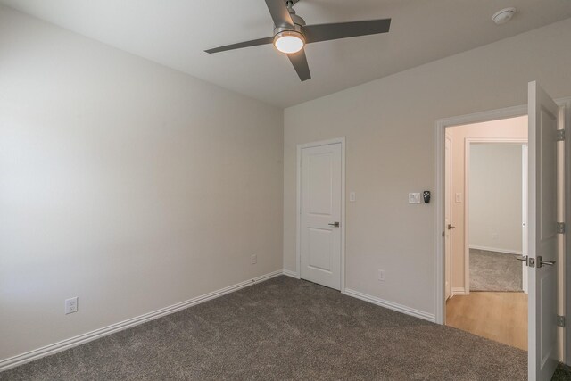 empty room featuring a ceiling fan, dark carpet, and baseboards