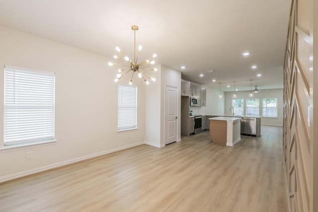 kitchen with appliances with stainless steel finishes, open floor plan, a center island, hanging light fixtures, and light countertops