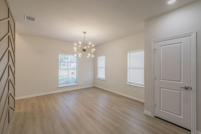 spare room with light wood-type flooring and a notable chandelier