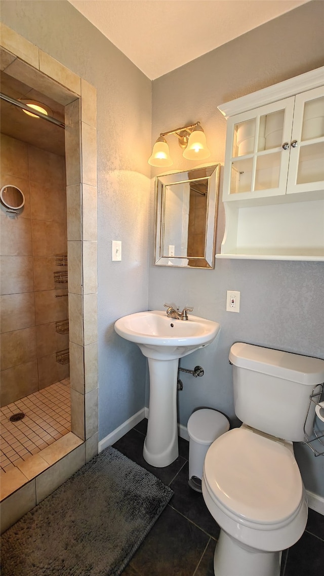 bathroom featuring toilet, sink, tile patterned flooring, and tiled shower