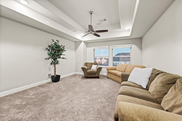 living area featuring carpet flooring, baseboards, visible vents, a raised ceiling, and a ceiling fan