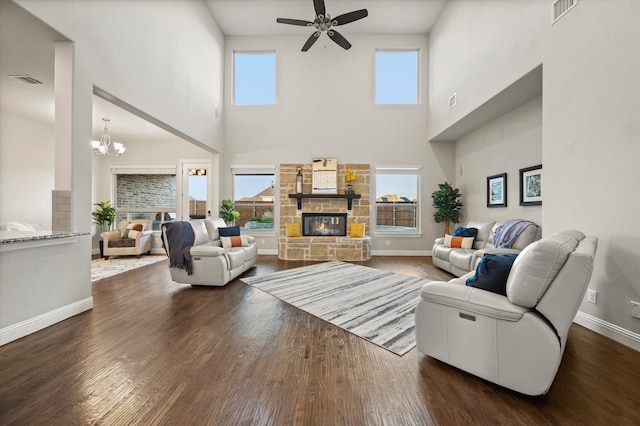 living room with a high ceiling, ceiling fan with notable chandelier, dark hardwood / wood-style floors, and a stone fireplace