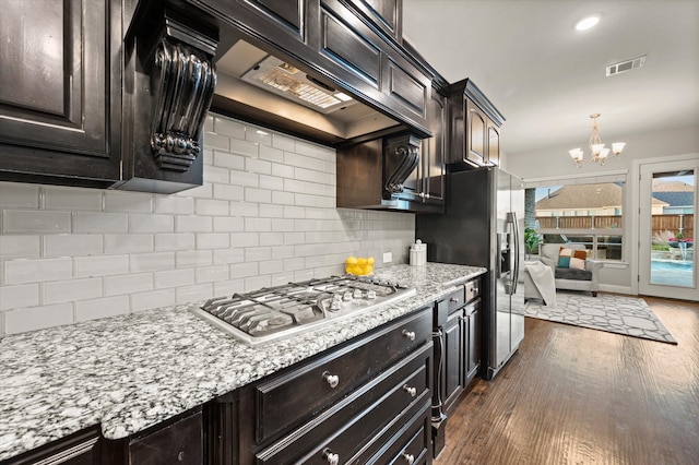 kitchen featuring stainless steel gas stovetop, custom exhaust hood, dark wood-type flooring, an inviting chandelier, and tasteful backsplash