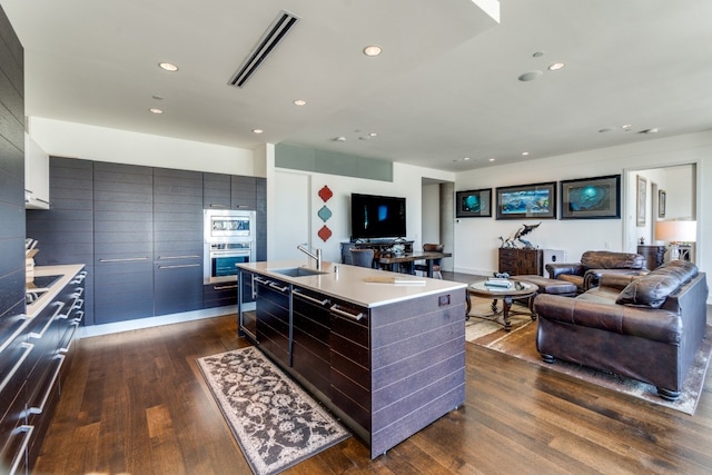 kitchen featuring appliances with stainless steel finishes, sink, dark wood-type flooring, and an island with sink