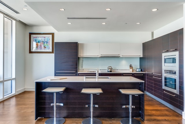 kitchen with a center island with sink, a kitchen breakfast bar, dark hardwood / wood-style floors, white cabinetry, and stainless steel appliances