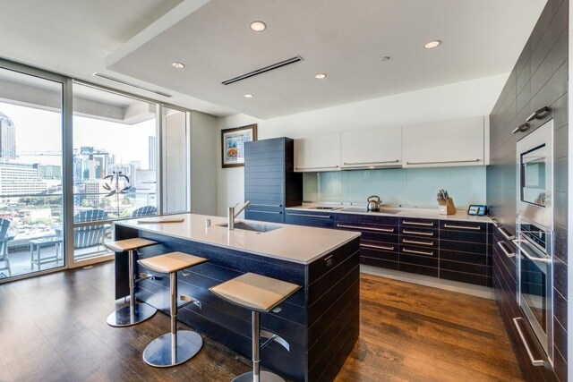 kitchen featuring white cabinetry, sink, stainless steel appliances, dark hardwood / wood-style flooring, and a kitchen island with sink