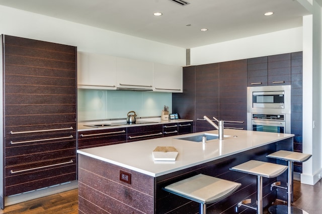 kitchen featuring sink, dark wood-type flooring, a kitchen island with sink, a breakfast bar, and appliances with stainless steel finishes