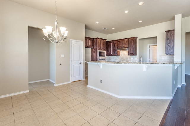 kitchen with stainless steel microwave, an inviting chandelier, tasteful backsplash, light stone counters, and kitchen peninsula