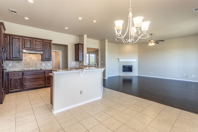 kitchen featuring light stone countertops, backsplash, ceiling fan with notable chandelier, light tile patterned floors, and a fireplace