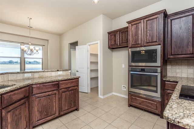 kitchen featuring built in microwave, stainless steel oven, an inviting chandelier, light stone counters, and decorative backsplash