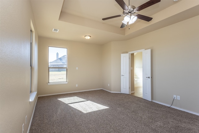 carpeted spare room with ceiling fan and a raised ceiling