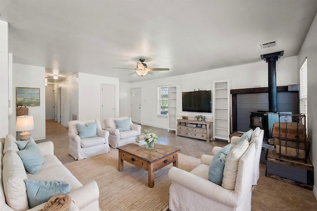 tiled living room featuring ceiling fan and a wood stove