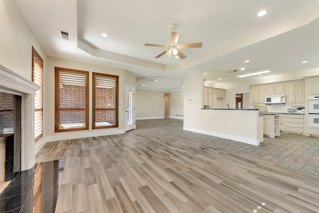 unfurnished living room featuring a tray ceiling, light hardwood / wood-style floors, and ceiling fan