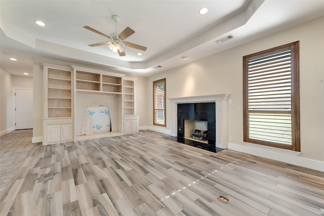 unfurnished living room with a raised ceiling, ceiling fan, and light hardwood / wood-style flooring