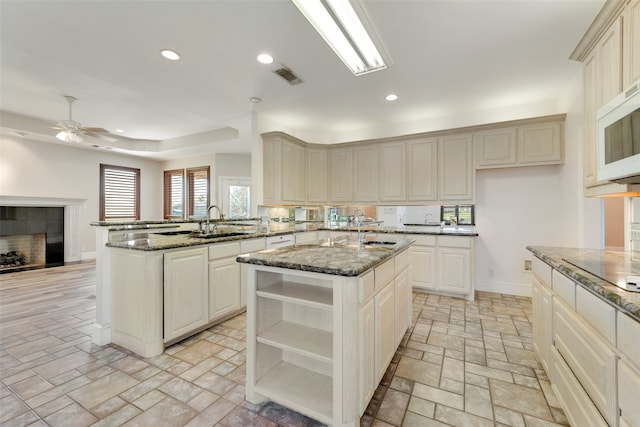 kitchen with dark stone countertops, sink, kitchen peninsula, and an island with sink