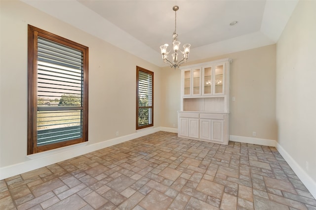 spare room featuring a raised ceiling and a chandelier