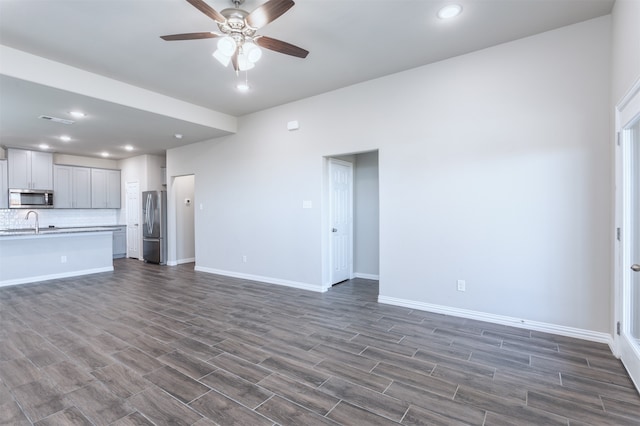 unfurnished living room with ceiling fan, sink, and dark wood-type flooring