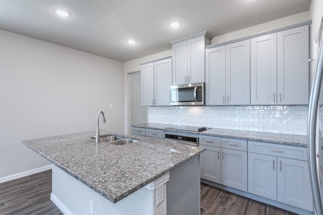 kitchen featuring light stone countertops, dark hardwood / wood-style flooring, stainless steel appliances, sink, and an island with sink