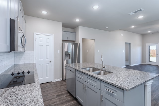 kitchen featuring light stone countertops, sink, dark wood-type flooring, a center island with sink, and appliances with stainless steel finishes