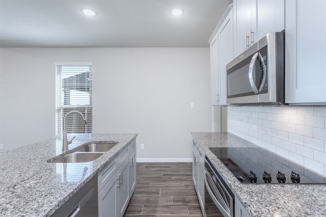 kitchen with sink, dark hardwood / wood-style floors, decorative backsplash, light stone counters, and stainless steel appliances