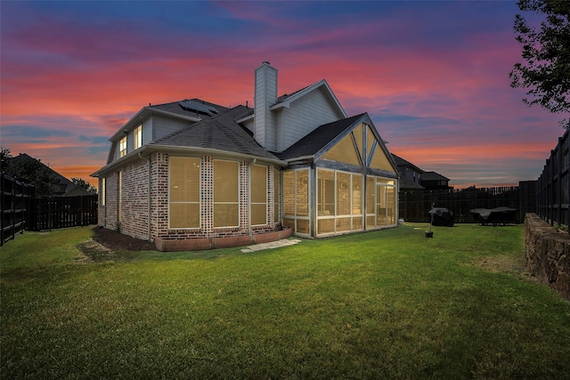 back house at dusk featuring a yard and a sunroom