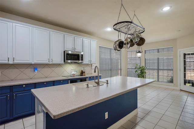 kitchen with white cabinetry, an island with sink, hanging light fixtures, and blue cabinets