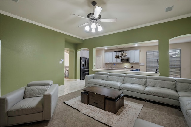 carpeted living room with ceiling fan, ornamental molding, and sink