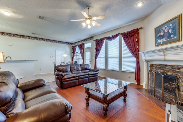 living room with ceiling fan, a fireplace, wood-type flooring, and a textured ceiling