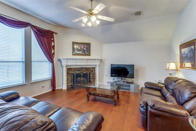 living room with lofted ceiling, hardwood / wood-style flooring, ceiling fan, a fireplace, and a textured ceiling