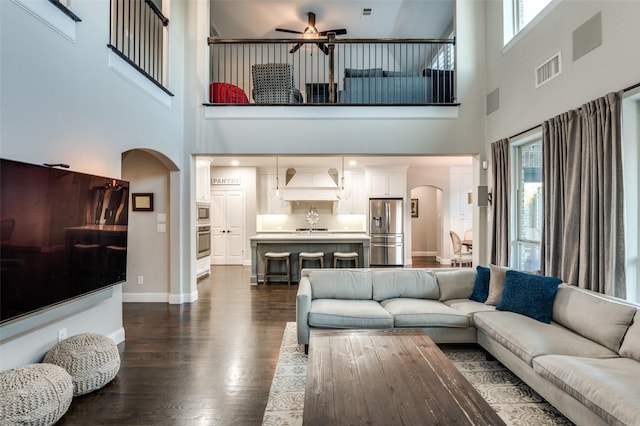 living area with arched walkways, a ceiling fan, visible vents, baseboards, and dark wood-style floors