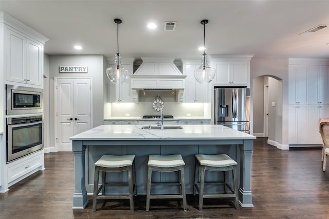 kitchen with white cabinets, appliances with stainless steel finishes, hanging light fixtures, and custom exhaust hood