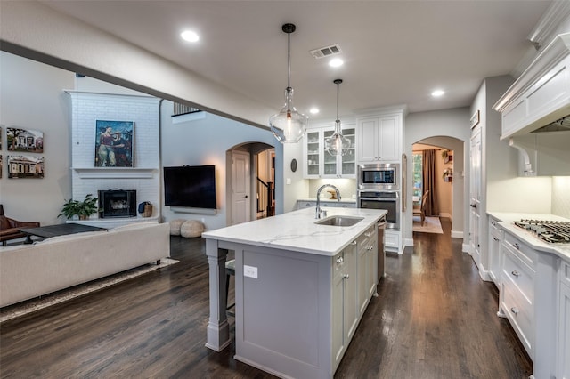 kitchen featuring glass insert cabinets, arched walkways, open floor plan, and a sink