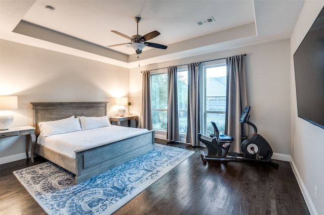 bedroom with dark hardwood / wood-style floors, a raised ceiling, and ceiling fan