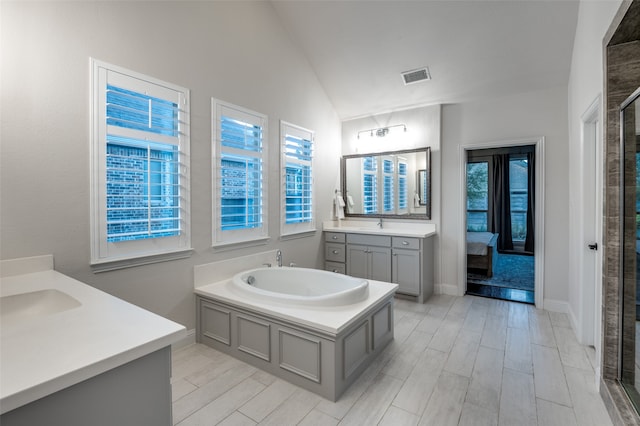 ensuite bathroom with wood finish floors, two vanities, visible vents, vaulted ceiling, and a sink