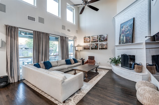 living room with a towering ceiling, a brick fireplace, ceiling fan, and dark wood-type flooring