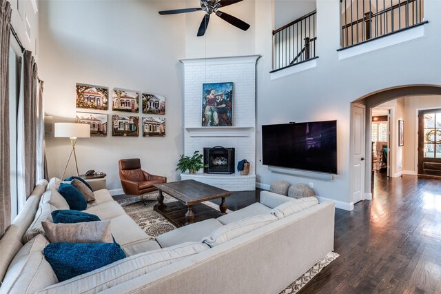 living room featuring a fireplace, a high ceiling, dark hardwood / wood-style flooring, and ceiling fan