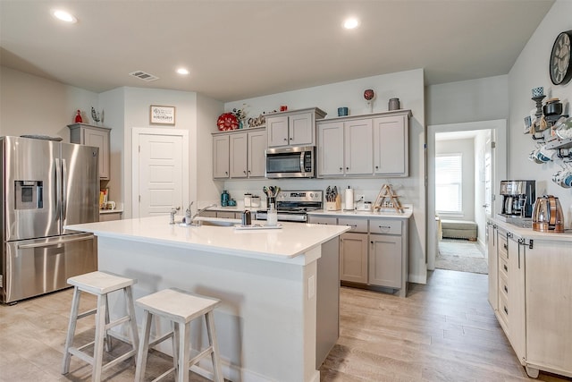 kitchen with gray cabinetry, sink, light hardwood / wood-style floors, a breakfast bar, and appliances with stainless steel finishes