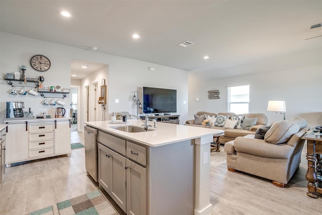 kitchen with light hardwood / wood-style floors, stainless steel dishwasher, a kitchen island with sink, and sink