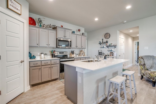 kitchen with a kitchen bar, sink, light hardwood / wood-style floors, and appliances with stainless steel finishes