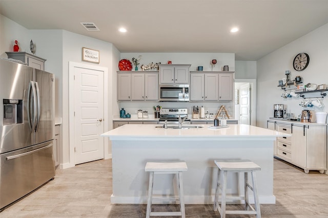 kitchen featuring sink, an island with sink, light hardwood / wood-style floors, a kitchen bar, and stainless steel appliances