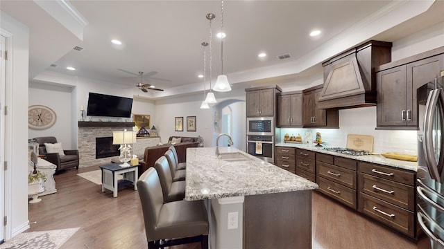 kitchen with light stone countertops, an island with sink, wood-type flooring, a fireplace, and a breakfast bar