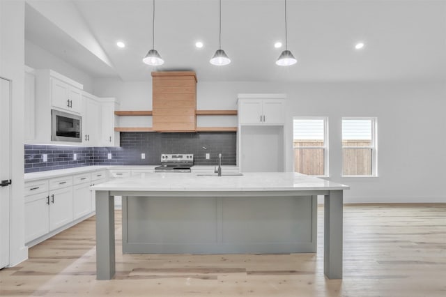 kitchen featuring decorative light fixtures, a center island with sink, stainless steel range with electric cooktop, and vaulted ceiling